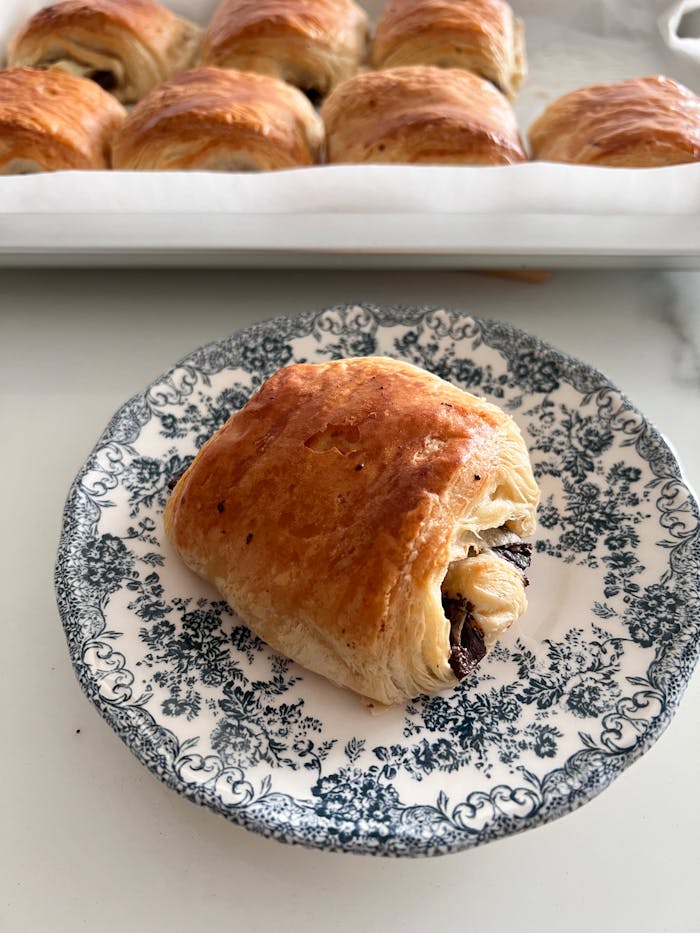 Freshly baked chocolate croissant on a decorative plate, showcasing rich, flaky pastry texture and enticing chocolate filling.
